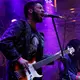 Artur Ferreira, aluno do Curso Córtex e engenheiro de materiais, tocando guitarra e cantando em um show ao vivo sob iluminação roxa.